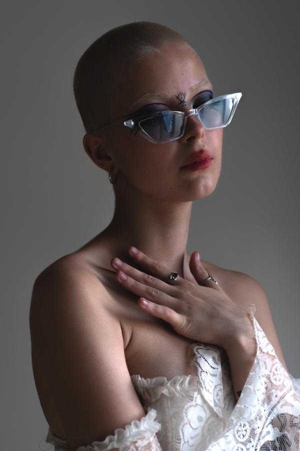 Portrait au crâne rasé, lunettes bleues et rouge à lèvres, la main sur la poitrine — photographie de Claude Quéré