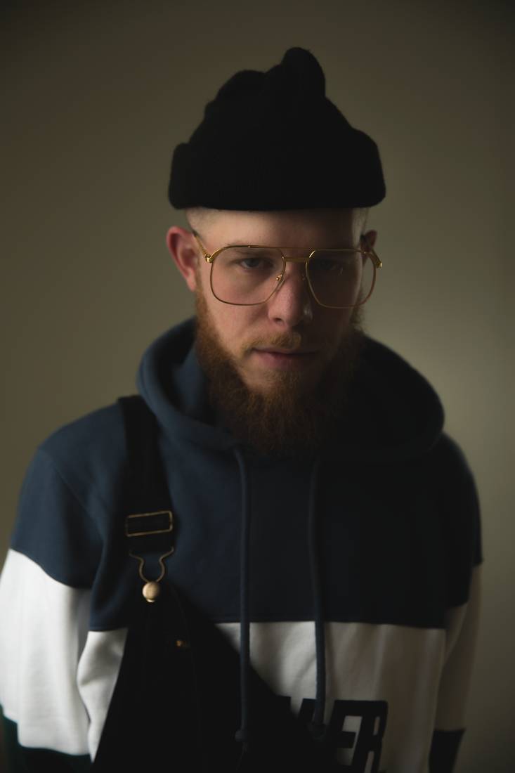 Portrait masculin au bonnet et lunettes dorées, sac bandoulière — photographie de Claude Quéré
